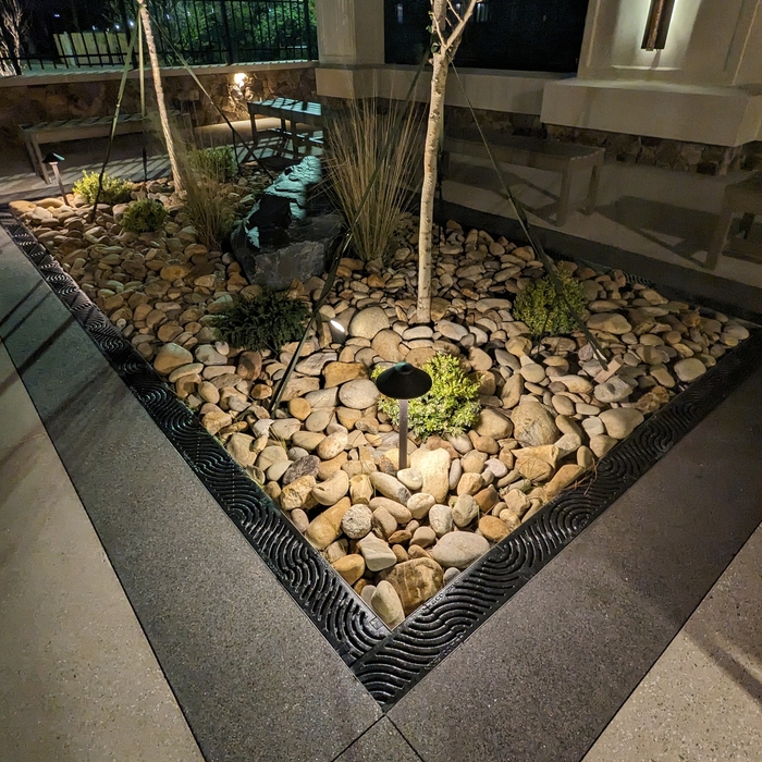 An up close view of the detailed SandX paving in conjunction with the intricate drain system. The planting beds features 2 matched Ginko trees along with a black slate boulder and low level plantings. The downlights provide safe viewing at night