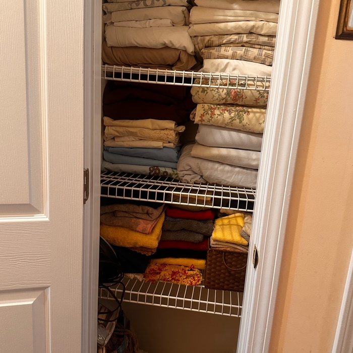 The picture displays a linen closet that has been expertly re-organized, with towels and linens neatly folded and precisely stacked, showcasing a serene and orderly arrangement. The thoughtful organization ensures easy access and maximizes the use of space.