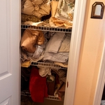 The picture captures a linen closet before organization, where towels and linens appear haphazardly placed, with items cluttering the shelves and little sense of order. The space seems overcrowded and chaotic, making it challenging to locate specific items or efficiently use the available storage area.