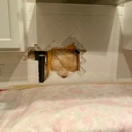 Removing the tile to access the pipes in the wall to locate a hot water line.
