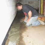 One of our crew members replaces the concrete slab. The miradrain is visible along the left perimeter as well as the plastic vapor barrier placed over the gravel. This helps prevent moisture from working thru the concrete during periods of heavy rain.