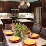 This kitchen previously had oak cabinets, white appliances & an aging tile floor. I was able to save the existing cabinets, & my client considerable money in not having to replace them, by having them stripped & stained, then added sleek handles & door pulls to complete the contemporary update. The new stainless steel appliances play off the cabinet hardware and the new brushed stainless steel backsplash.