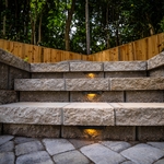 Shown are the riser steps leading to the upper level paver patio that was tiered by the retaining wall. We installed lighting along these steps which really creates an amazing look and atmosphere at night time for you, family, and friends to enjoy!