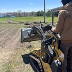Mini skid steer pushing around dirt.