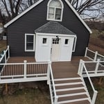 Full front view of the home after renovation, showcasing new slate-colored CertainTeed Restoration Classic siding with crisp white board and batten on the front gable and entryway. The rebuilt porch features Trex Basics Toasted Sand decking, accented with white trim and aluminum railings for a modern, maintenance-free finish.