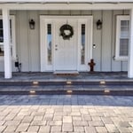 An elegant modern farmhouse front porch with concrete pavers and low-voltage lighting
