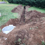 Excavate trench through yard to the well to holding tank that serves the customers house.