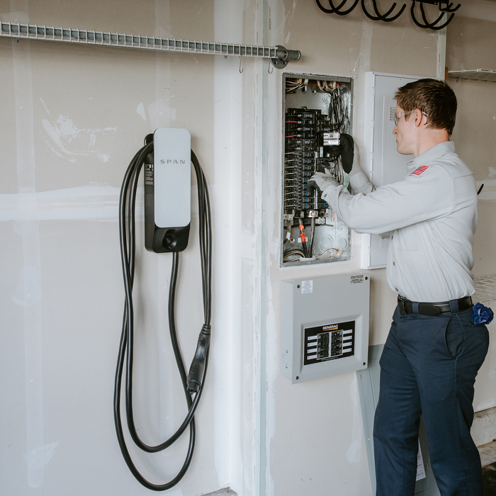 Elektricien werkt aan elektrische groepenkast naast laadvoorziening voor elektrische auto