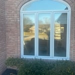 A stunning arched window with three vertical panels, framed in bright white trim and set in a rich red brick exterior. This elegant design captures ample natural light and creates a sophisticated focal point on the home’s front façade, paired with neatly manicured landscaping.