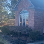 A broader view of the arched window from a distance, showcasing how the updated window design enhances the architecture of the home. Framed by a brick gable, detailed trim, and mature landscaping, this window serves as a beautiful statement piece that elevates the entire property’s exterior appeal.