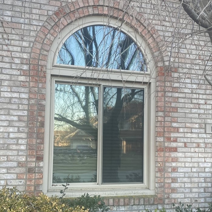 This photo features a beautifully designed arched window with a classic brick surround. The large window includes a rectangular double-pane bottom section with a decorative arched transom above, framed in neutral beige.