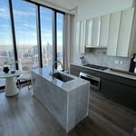 This contemporary high-rise kitchen renovation pairs two-tone handless cabinetry with a light stone waterfall island, built-in stainless steel appliances and an undermount sink. The compact layout adds valuable prep space, storage and casual seating while preserving the natural light and skyline views, an effective solution for a New York City condo or apartment.