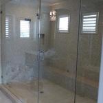 a large frameless glass shower with glass mosaic tiled walls and a square windows offering natural light