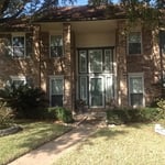 a two story home exterior with beige brick siding, white trimmed windows and front yard landscaping