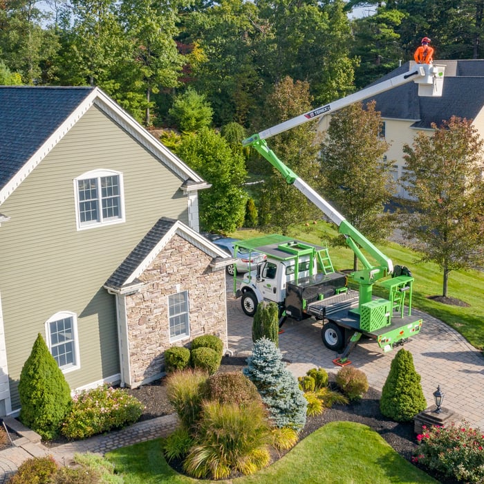 Tree service bucket truck and arborist working beside a residential home during a professional pruning visit
