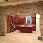 a unique biege brick accent wall with an arched entrance into kitchen
