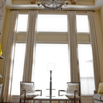 The large windows are the focal point of this gorgeous living room with a high coffered ceiling, beautiful wrought iron chandelier ,soft yellow walls and lovely spindle chairs.