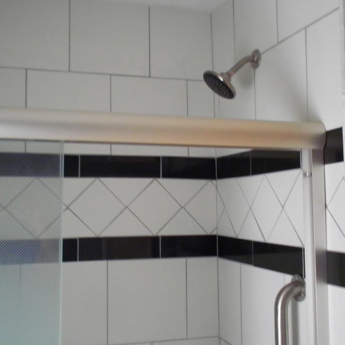 a black and white tiled shower wall with a framed glass shower door and brushed nickel finish fixtures