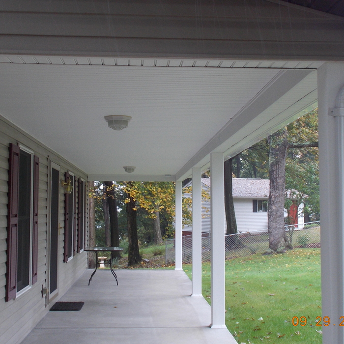 Home exterior with tan vinyl siding, red window shutters, and concrete patio