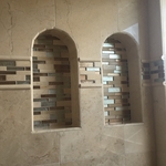 Bathroom with polished travertine tile walls, tiled shower niche, and mosaic tile accents
